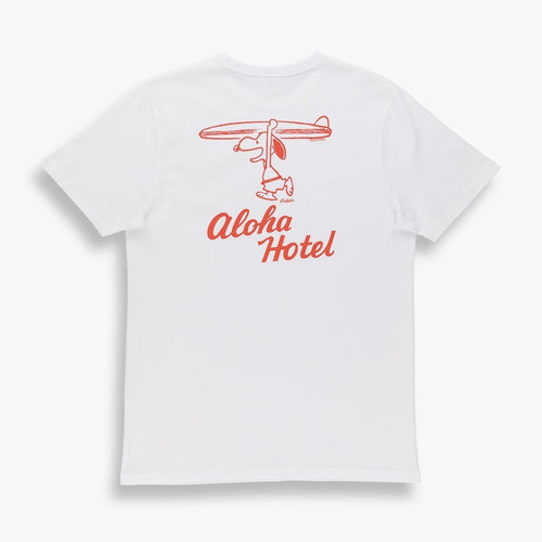 White shirt with a design of snoopy holding a surfboard over his head. The words aloha hotel written underneath it in red. 