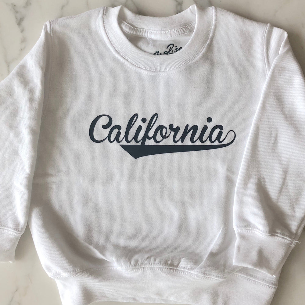 On The Rise CALIFORNIA Pullover Sweatshirt. White sweatshirt with black text stating California in cursive text