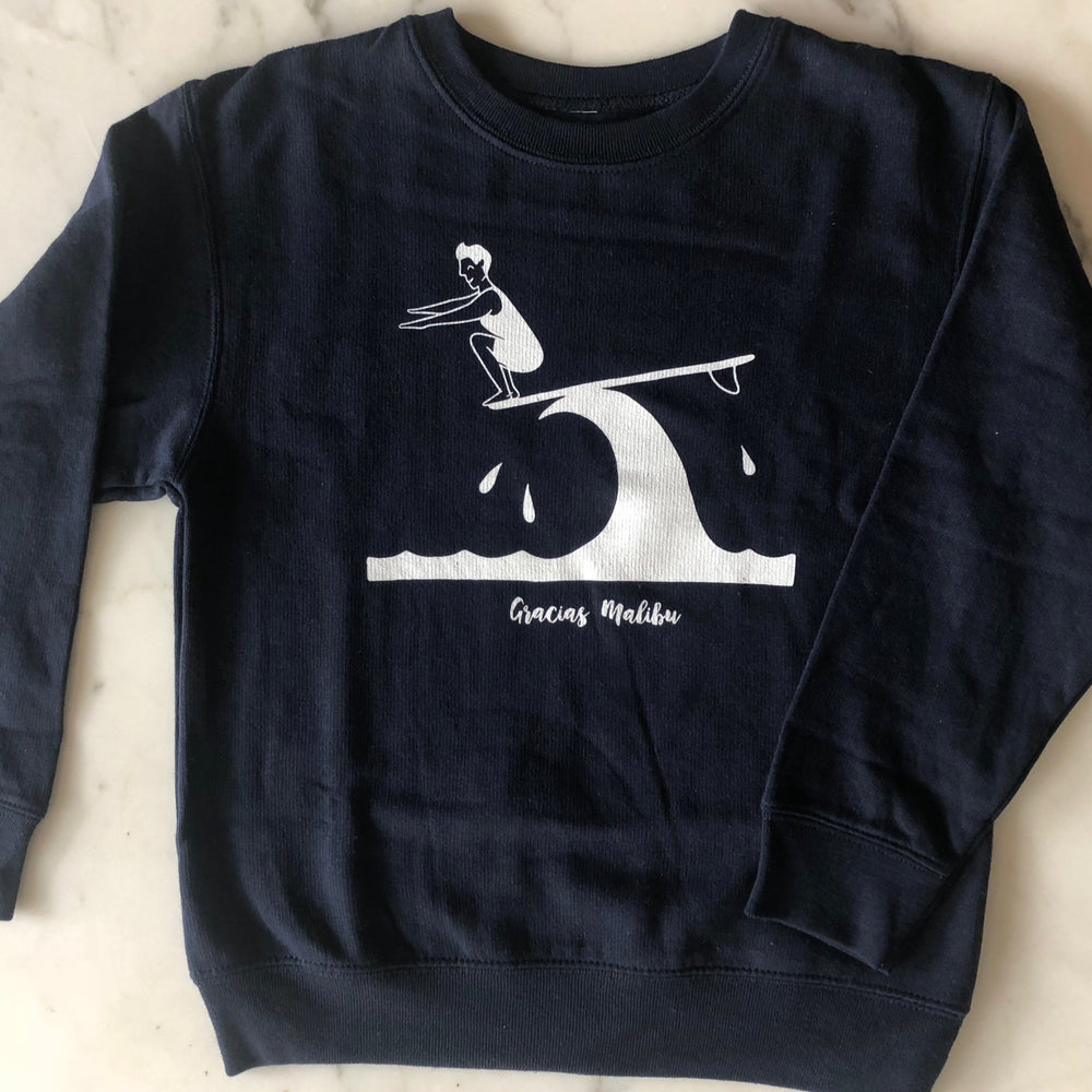 Gracias Malibu black sweatshirt with a white print design of a man surfing on a wave crouching down at the end of a surfboard. The text at the bottom reads gracias Malibu. 