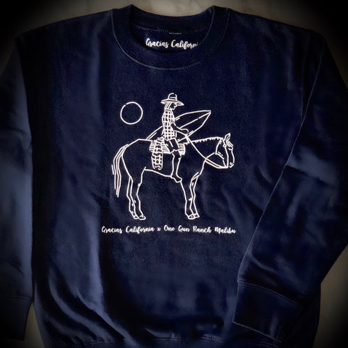 GC kids navy sweatshirt with a white outline of a woman riding a horse and holding a surfboard. At the bottom the text says gracias california X one gun ranch malibu. 