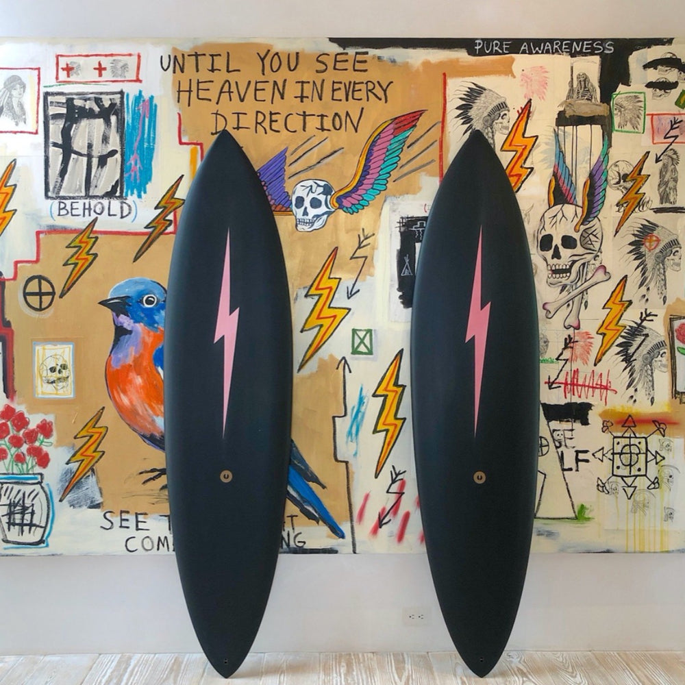 Two solid black surfboards with a long blush pink lightning bolt down the middle. 