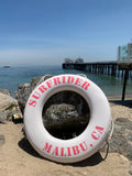 White lifesaver with the words Surfrider Malibu, CA in pink around it. 