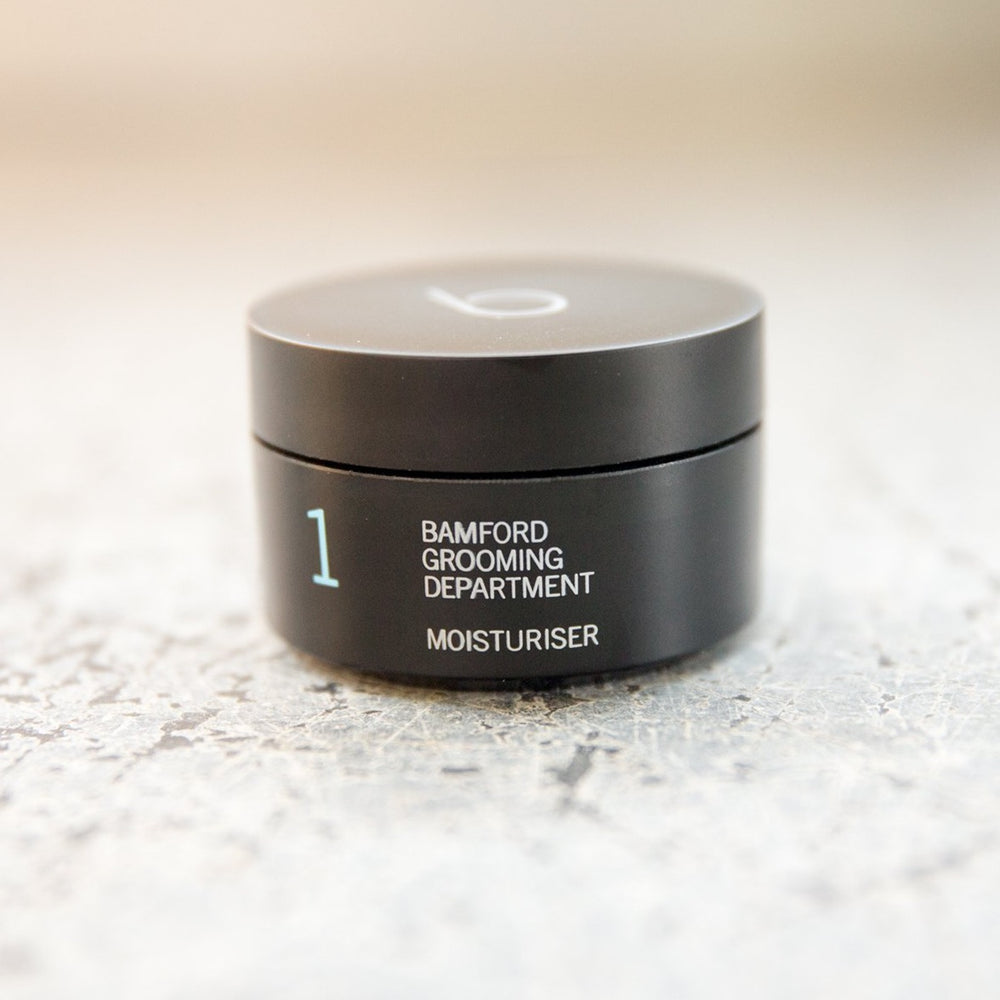 A black canister with a black twist on lid. On it says bamford grooming department moisturiser 1. 