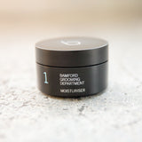 A black canister with a black twist on lid. On it says bamford grooming department moisturiser 1. 