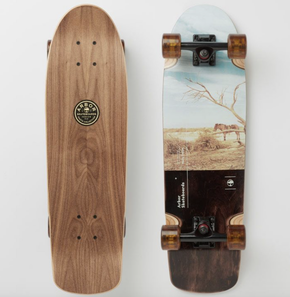 The left shows the top of the board. It is a brown wood grain with the logo ARBOR Skateboards in the top center. The left shows the bottom of the board. There is an image of a horse at a desert watering hole. The bottom has the logo Arbor Skateboards. The bearings are black and the wheels are a translucent brown. 