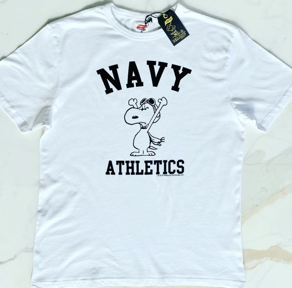 TSPTR Navy Athletics T-Shirt. White shirt with a design of Snoopy wearing aviator goggles on his head. The Words Navy Athletics prints next to him 