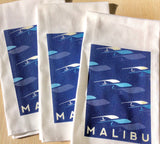One Gun Kitchen Towel. White fabric with a blue wave design and the word Malibu written in white text at the bottom. 