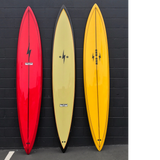 3 surfboards lined up. There's a red one on the left with a lightning bolt on the top center. The middle is a yellow board with black trim around the boarder. The right one is yellow with two lightning bolts and the logo One Gun in the middle. 