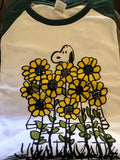 TSPTR Sunflowers Raglan T-Shirt. White shirt with green sleeves. It has a design of Snoopy in a field of tall sunflowers. 