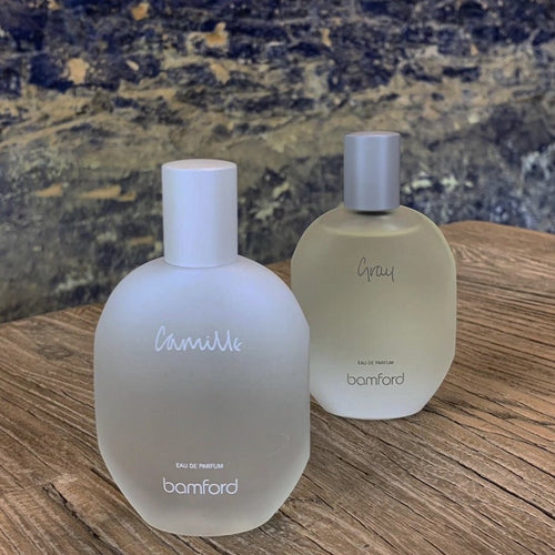 On the left is a frosted white glass bottow that says Bamford eau de perfum camille. On the right is a frosted light brown glass bottle with a gray twist on lif. It says Bamford eau du perfum gray. 