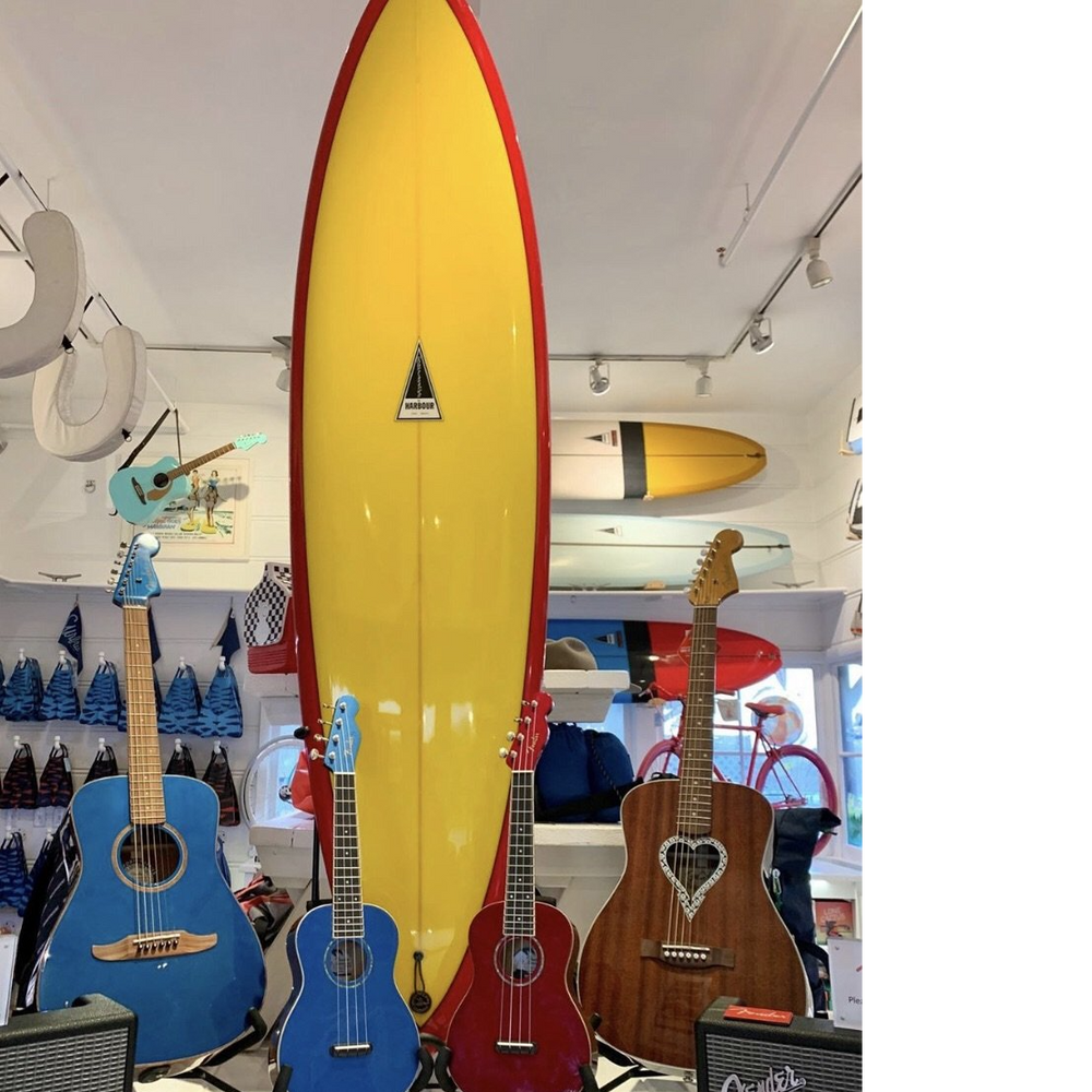 Yellow surfboard with a red trim around the boarder. The Harbour Surfboard is in the center inside a triangle design. 