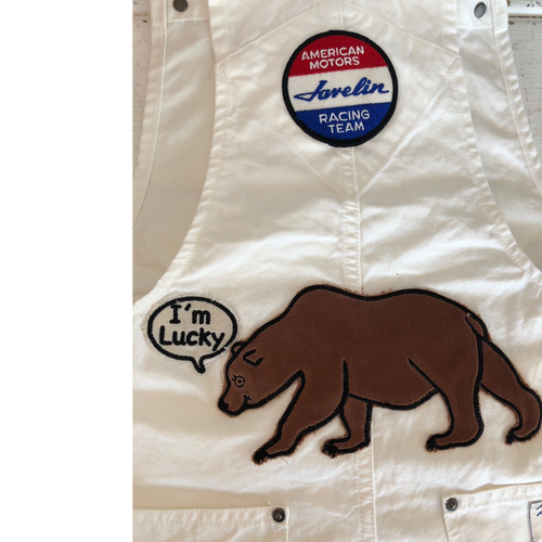 White denim overalls with an American motors racing team patch at the top. And a bear with a text bubble saying I'm Lucky on the bottom. 