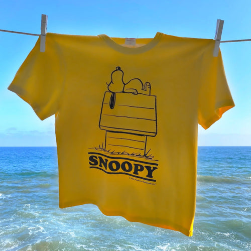 Yellow Peanuts Reduce Your Worries T-Shirt with a design of Snoopy laying on the top of his doghouse