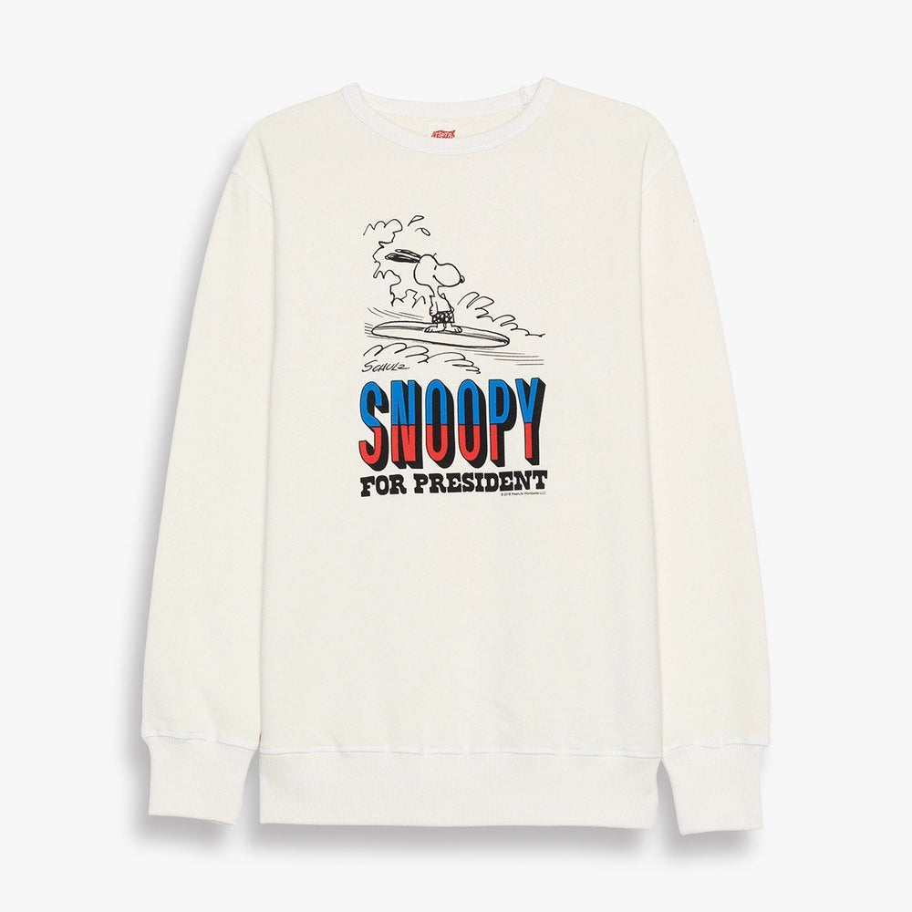 TSPTR Surfing Snoopy For President Sweatshirt. A white sweatshirt with a design of Snoopy riding a surfboard in the ocean. Below it it says Snoopy for President. 